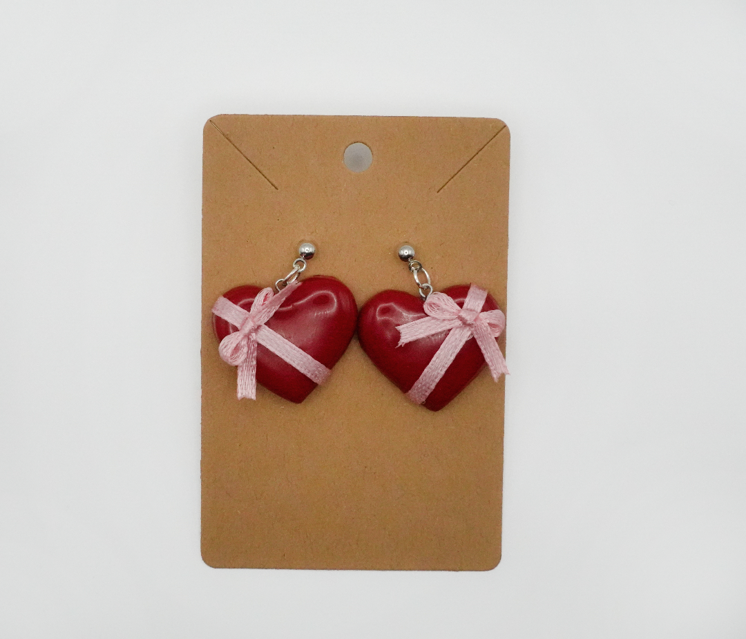 Elevate your everyday look with this stylish box of chocolate heart earrings. Featuring a pink ribbon detail. These versatile earrings are perfect for any occasion.
