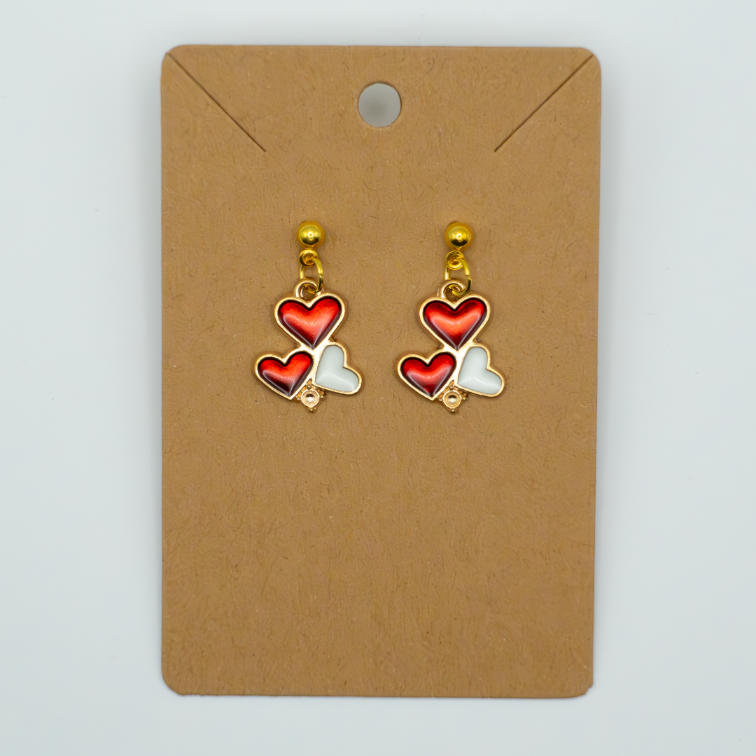 Celebrate love with these charming earrings featuring a cluster of red and white enamel hearts. Perfect for adding a touch of classic romance to any outfit.