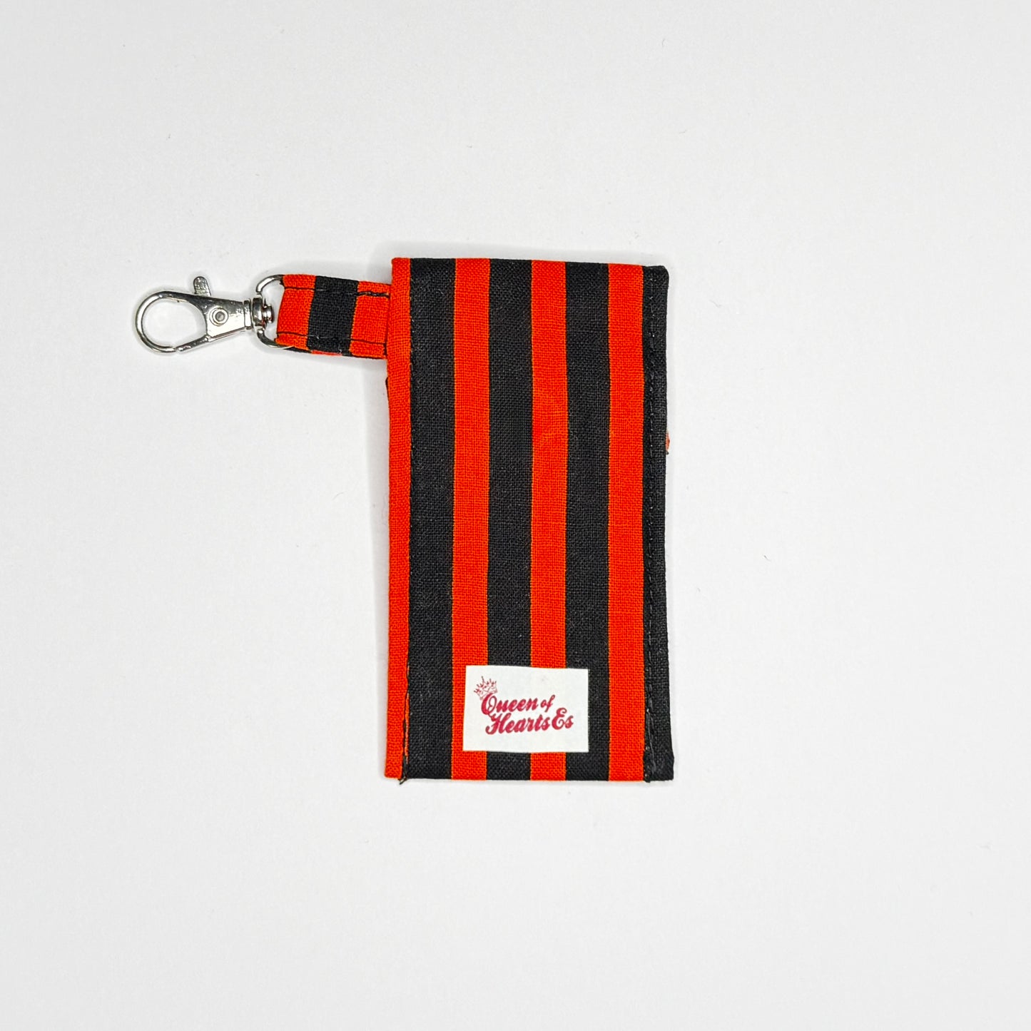 Keep your favorite lip color or balm secure and stylishly close at hand with this handmade fabric keychain pouch. Perfectly capturing a timeless rockabilly aesthetic, punk rock edge, and classic goth glamour, this compact accessory ensures you never lose your essentials at the bottom of your bag again.
This tailored fabric holder features a classic vertical stripe design in a high-contrast palette of vibrant orange and deep midnight black. Designed for ultimate everyday convenience, it includes a secure me