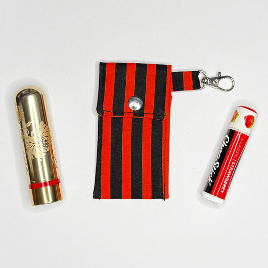 Keep your favorite lip color or balm secure and stylishly close at hand with this handmade fabric keychain pouch. Perfectly capturing a timeless rockabilly aesthetic, punk rock edge, and classic goth glamour, this compact accessory ensures you never lose your essentials at the bottom of your bag again.

This tailored fabric holder features a classic vertical stripe design in a high-contrast palette of vibrant orange and deep midnight black. Designed for ultimate everyday convenience, it includes a secure me