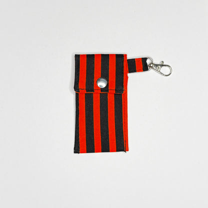 Keep your favorite lip color or balm secure and stylishly close at hand with this handmade fabric keychain pouch. Perfectly capturing a timeless rockabilly aesthetic, punk rock edge, and classic goth glamour, this compact accessory ensures you never lose your essentials at the bottom of your bag again.

This tailored fabric holder features a classic vertical stripe design in a high-contrast palette of vibrant orange and deep midnight black. Designed for ultimate everyday convenience, it includes a secure me