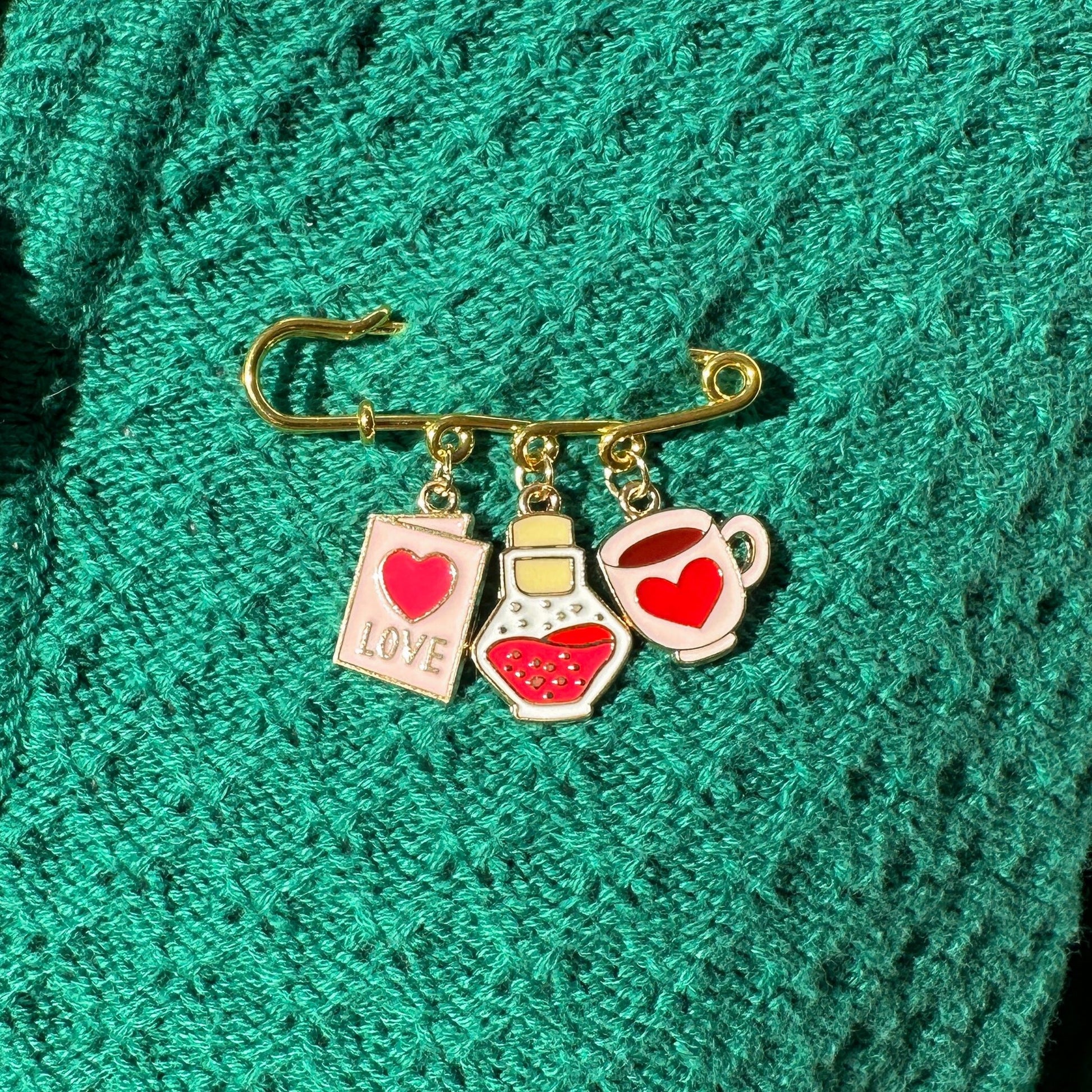 Elevate your Valentines Day or Galentines Day with this adorable gold iron pin brooch featuring love potion enamel charms. Perfect for adding a touch of love to any outfit.