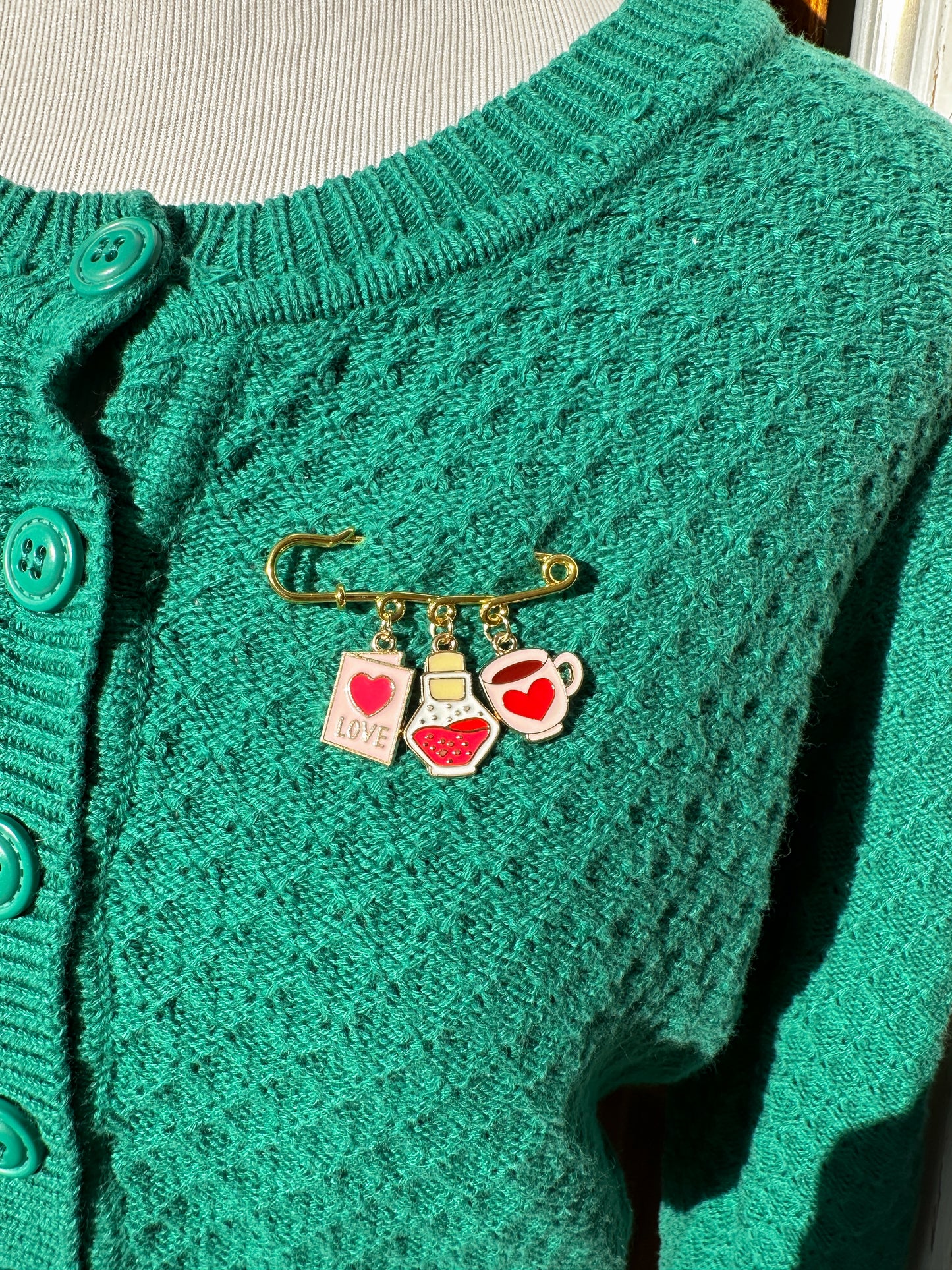 Elevate your Valentines Day or Galentines Day with this adorable gold iron pin brooch featuring love potion enamel charms. Perfect for adding a touch of love to any outfit.