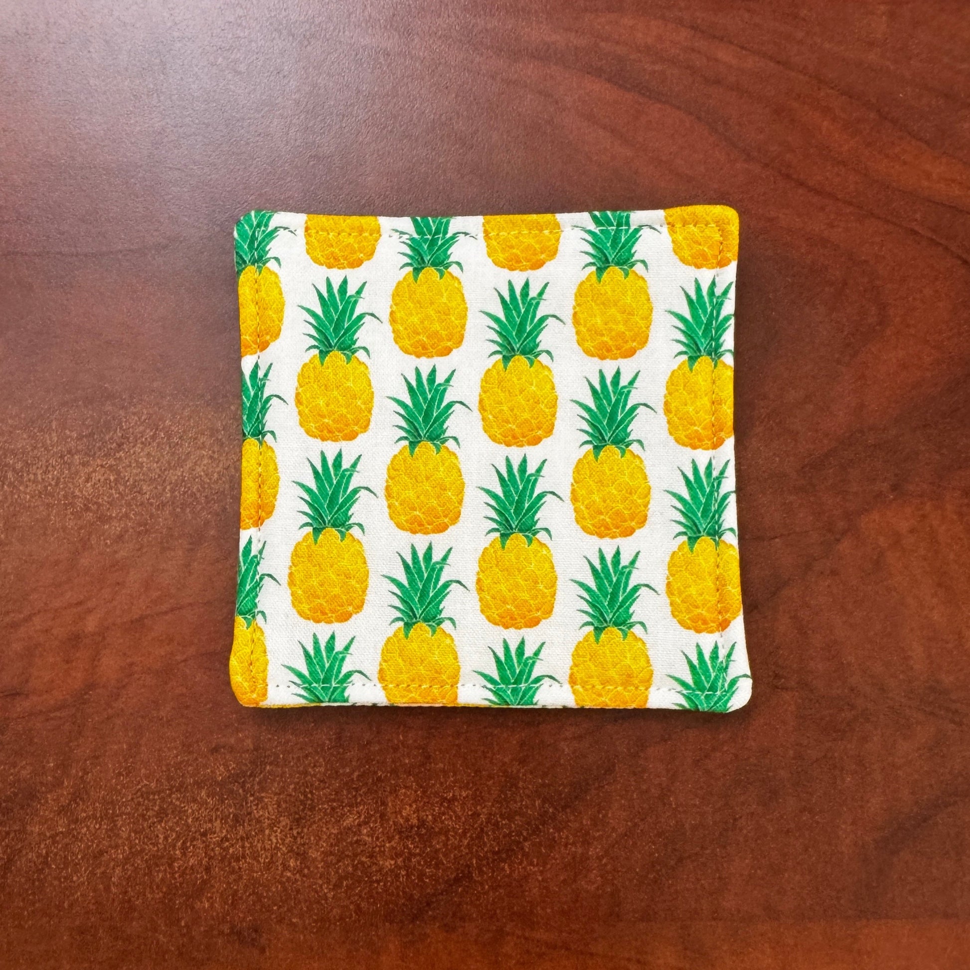 Keep your surfaces safe and stylish with our 100% cotton pineapple coaster. This charming coaster features a vibrant pineapple print that adds a touch of fresh, fruity fun to any room. Crafted with an absorbent cotton batting layer inside, it's designed to soak up condensation and protect your furniture from unsightly water rings and spills. Perfect for coffee mugs, glasses, or teacups, this durable and machine-washable coaster is a delightful addition to your kitchen or living room. Elevate your home decor