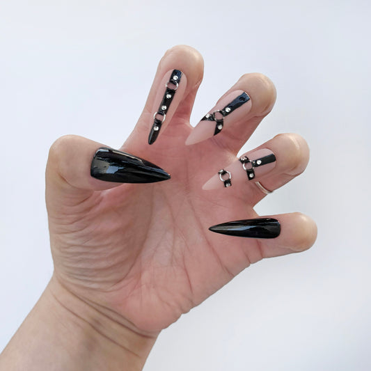 Get ready for "The Baddie" with these stunning, statement press-on nails. Featuring three nude base nails with harnesses and two all black nails to complete the look. Each set is a miniature work of art, meticulously designed and hand-painted, adding a unique flair to any occasion. No time for salon appointments? Say hello to instant glamour that’s ready whenever you are. Our durable, high-quality press-ons offer a flawless, comfortable fit and are designed to last.