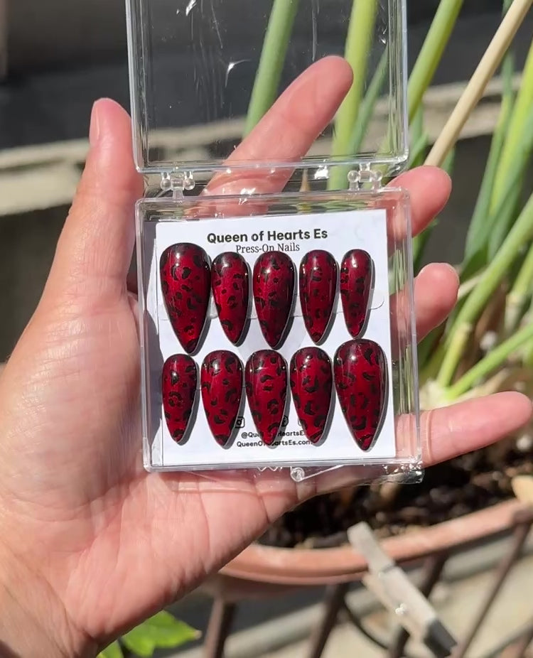 Get ready for "The Fierce Feline" and embrace dark glamour with these stunning handmade press-on nails, featuring a red cat eye base and delicate, black leopard design.&nbsp;